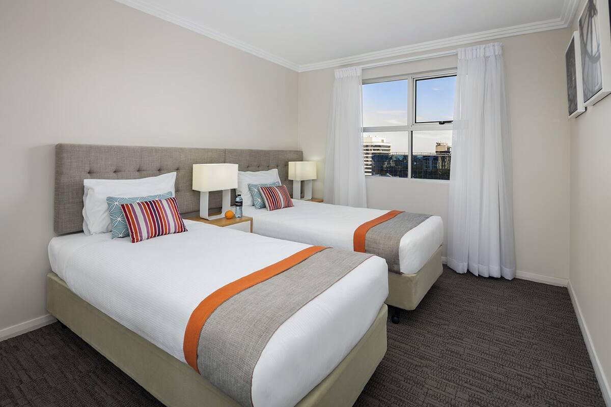 Une chambre d’hôtel avec deux lits, une grande fenêtre avec des rideaux et une vue sur la ville.