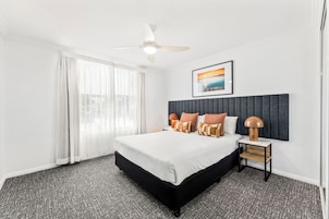A hotel room with a large bed, a ceiling fan, a nightstand with a lamp, and a framed picture on the wall.