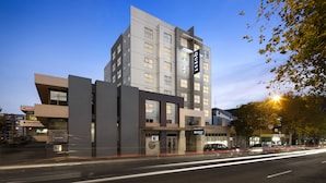 A modern hotel with a prominent 'QUEST' sign, a visible address, and a street view with passing traffic.