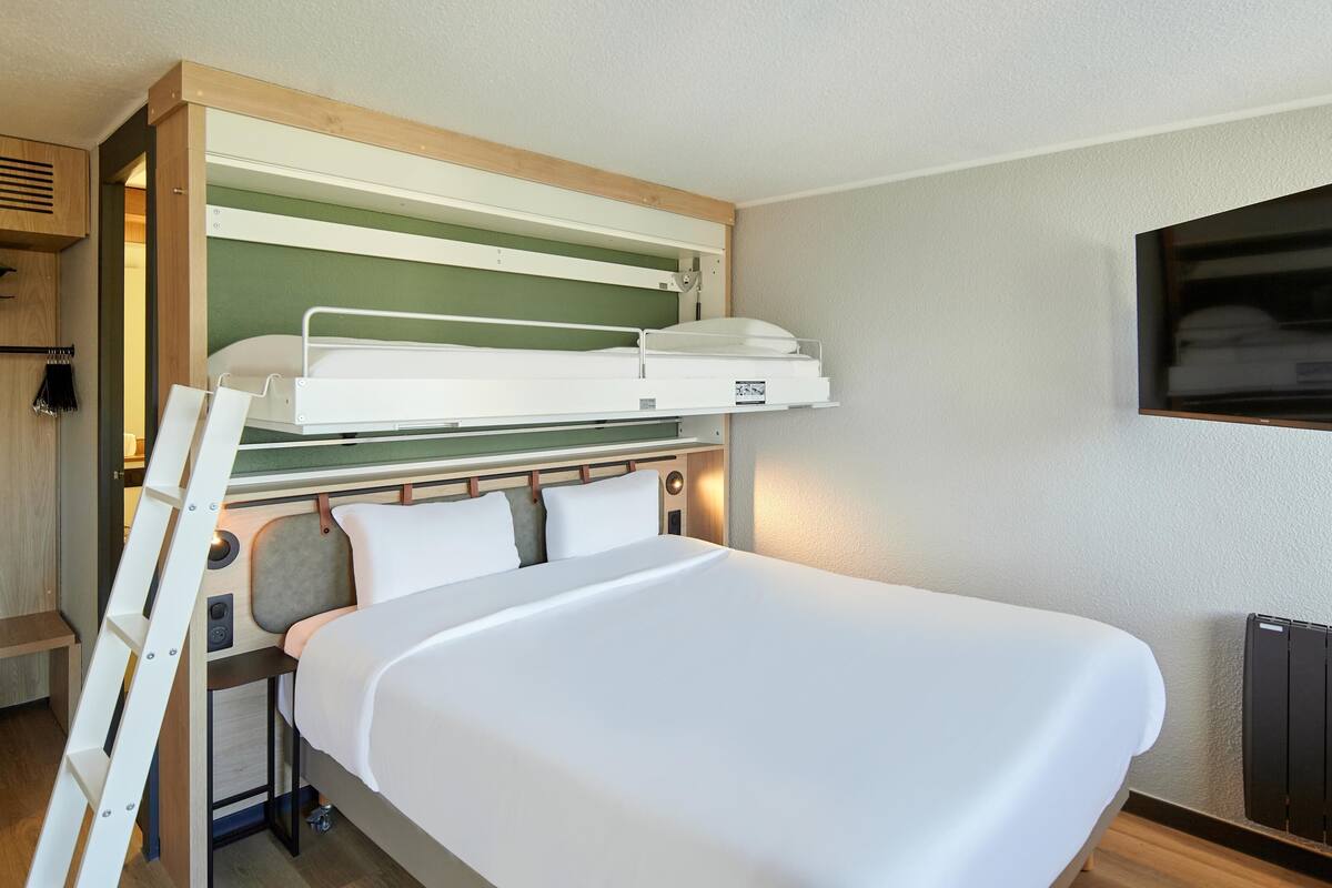 Une chambre d’hôtel compacte avec un lit superposé, un téléviseur à écran plat fixé au mur et un plancher en bois.