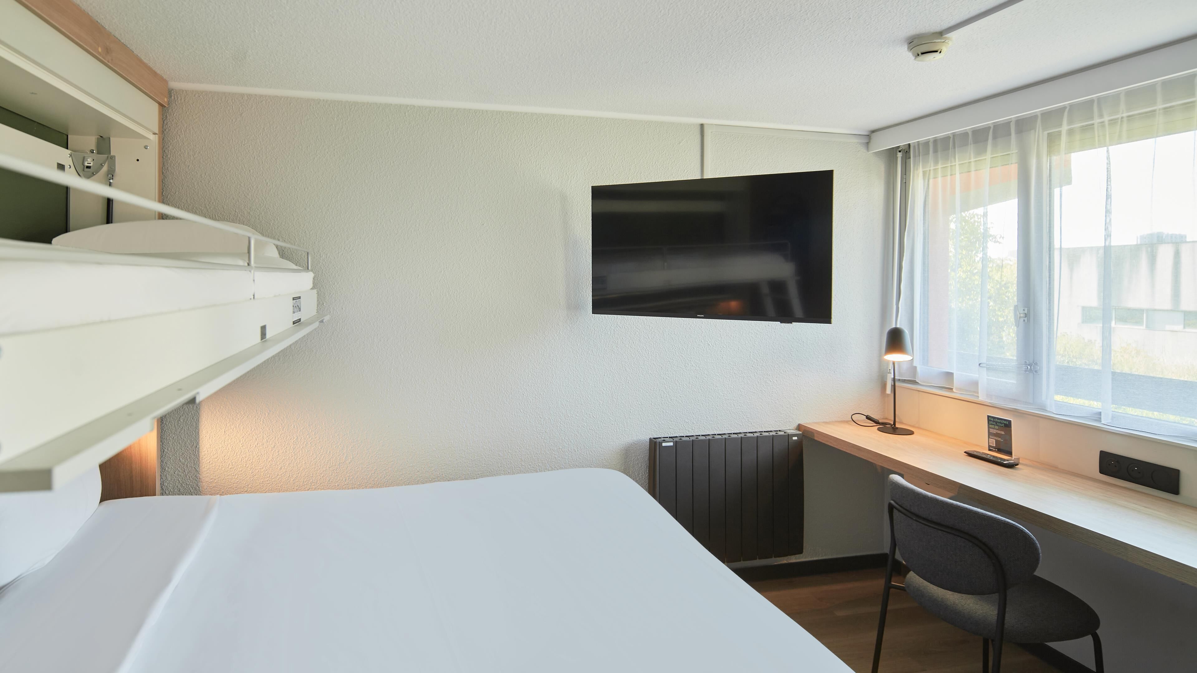Una habitación de hotel moderna con una cama, un escritorio, una silla, un televisor y una ventana con cortinas.