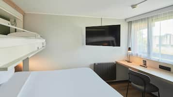 Una habitación de hotel moderna con una cama, un escritorio, una silla, un televisor y una ventana con cortinas.