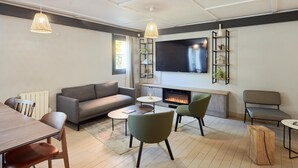 Un salon moderne comprenant un canapé, deux fauteuils, une table basse, une cheminée et un téléviseur fixé au mur.