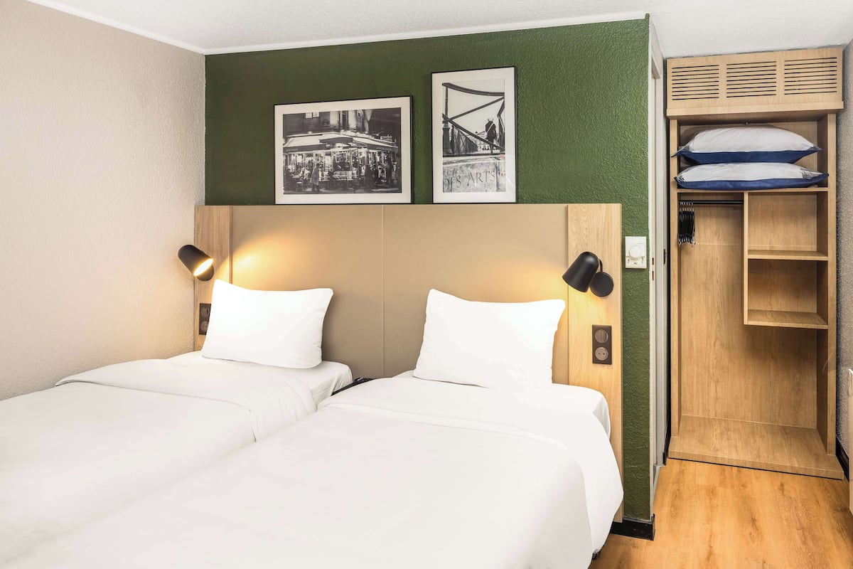 Une chambre d’hôtel avec deux lits, une armoire en bois et deux tableaux encadrés au mur.