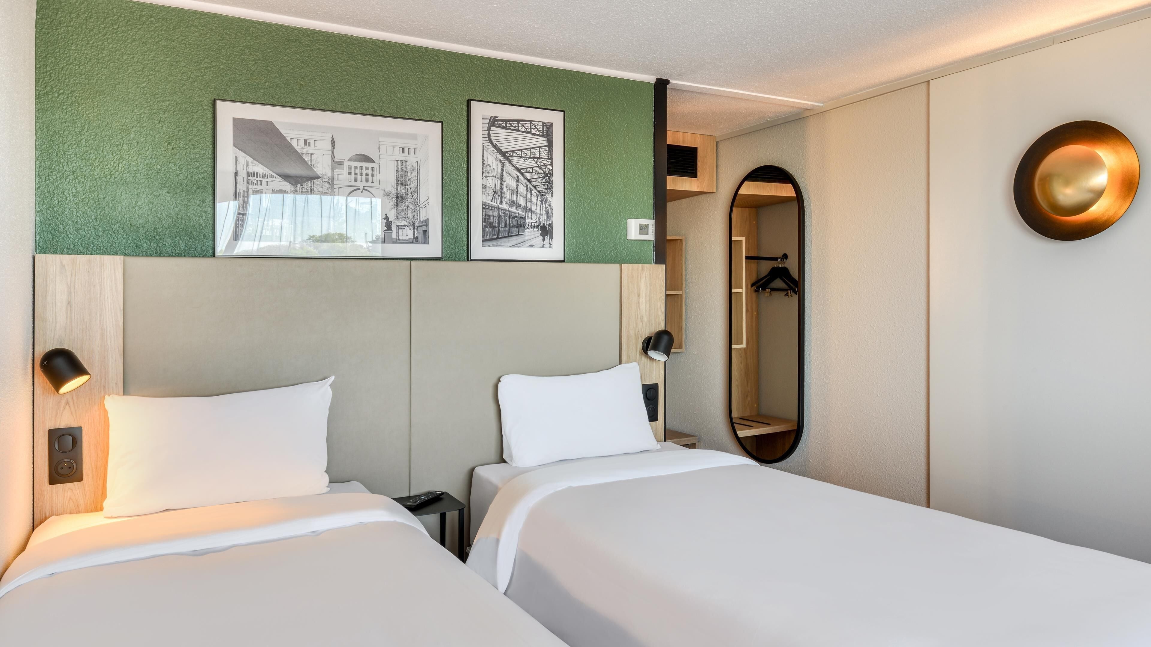 Habitación de hotel con dos camas, una pared verde con textura y un espejo con marco dorado.