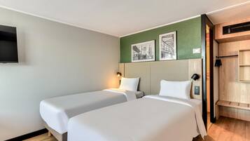 A hotel room with two beds, a flat-screen TV mounted on the wall, and a green accent wall with framed pictures.