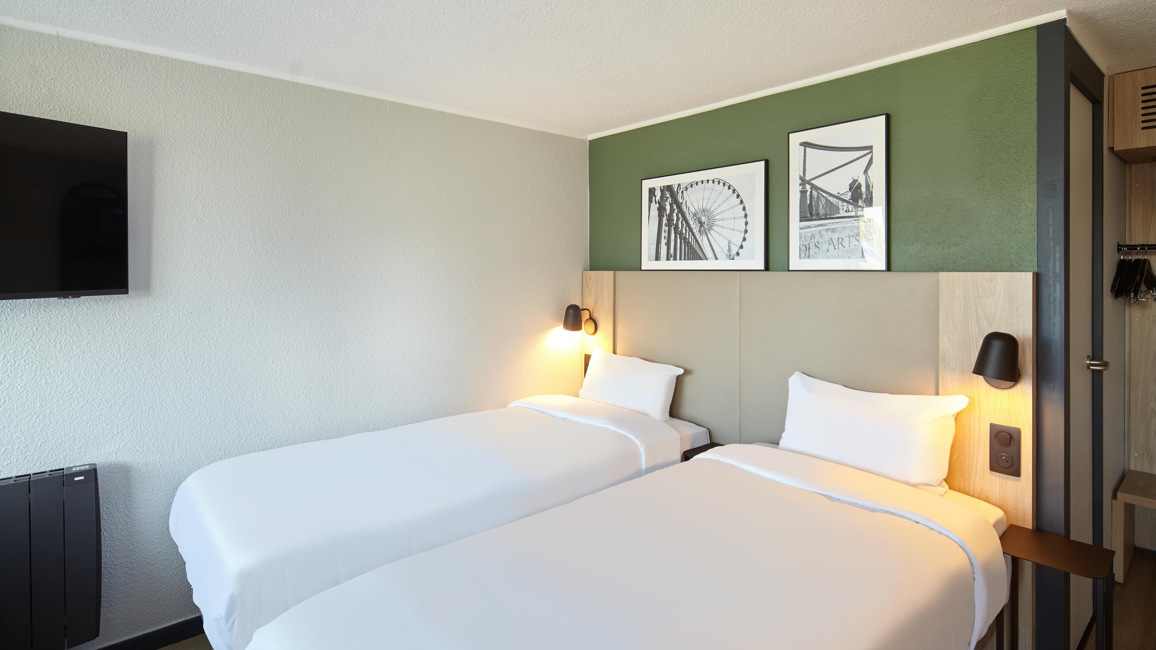 A hotel room with two beds, a flat-screen TV mounted on the wall, and two framed pictures above the beds.