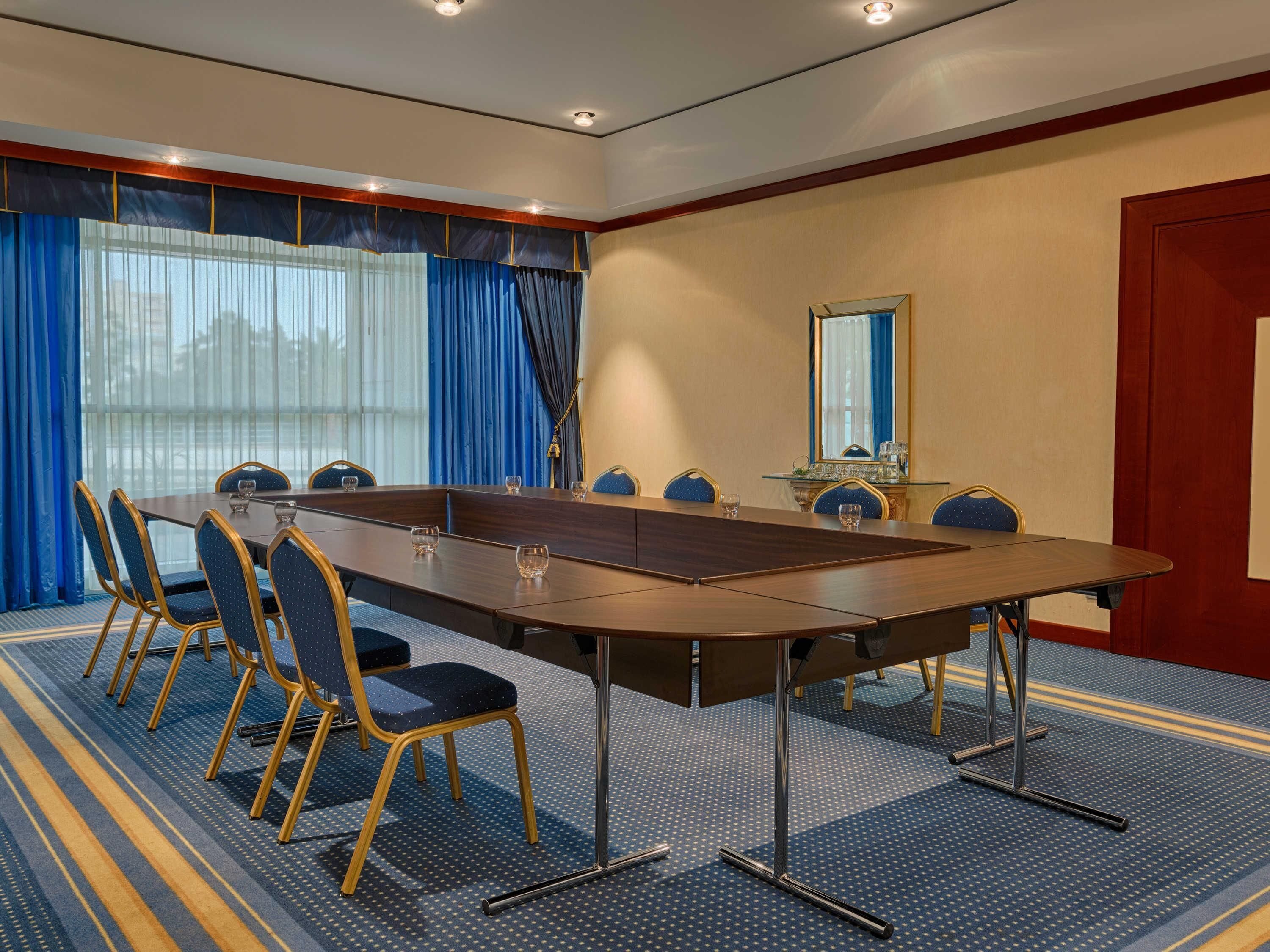 A conference room with a long table, chairs, a mirror, and a carpeted floor.