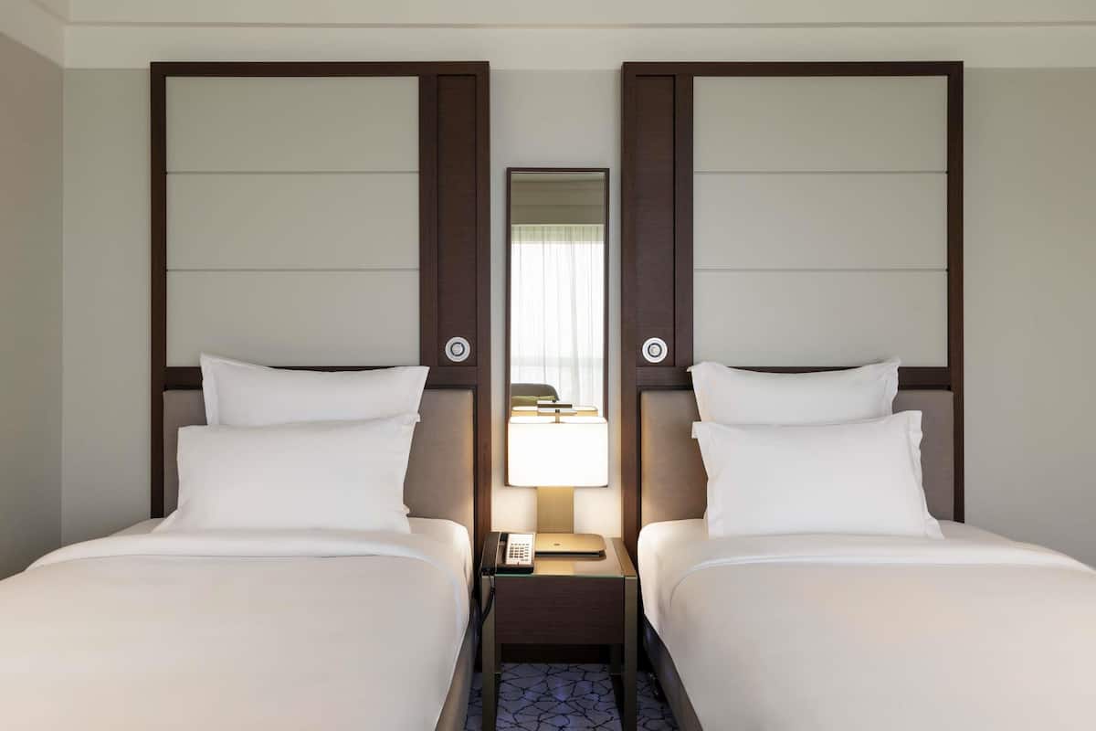 A hotel room with two beds, a nightstand with a lamp, and a mirror on the wall.