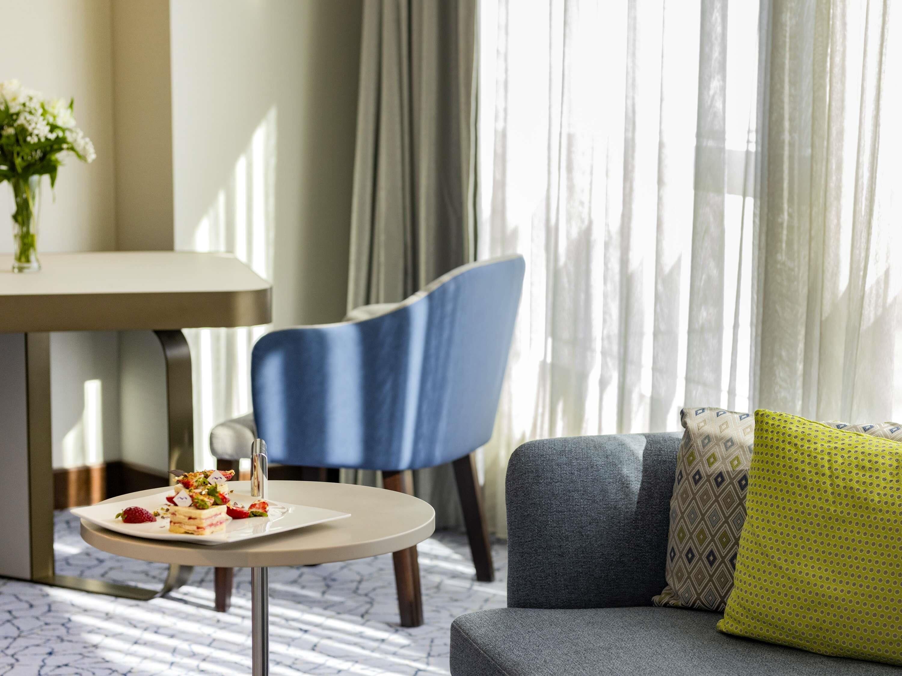 A modern hotel room with a dining area featuring a round table and a blue chair.