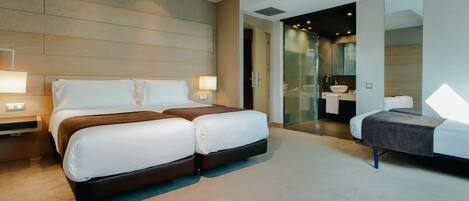 Una habitación de hotel moderna con una cama grande, una zona de estar separada y un baño visible a través de una puerta de vidrio.