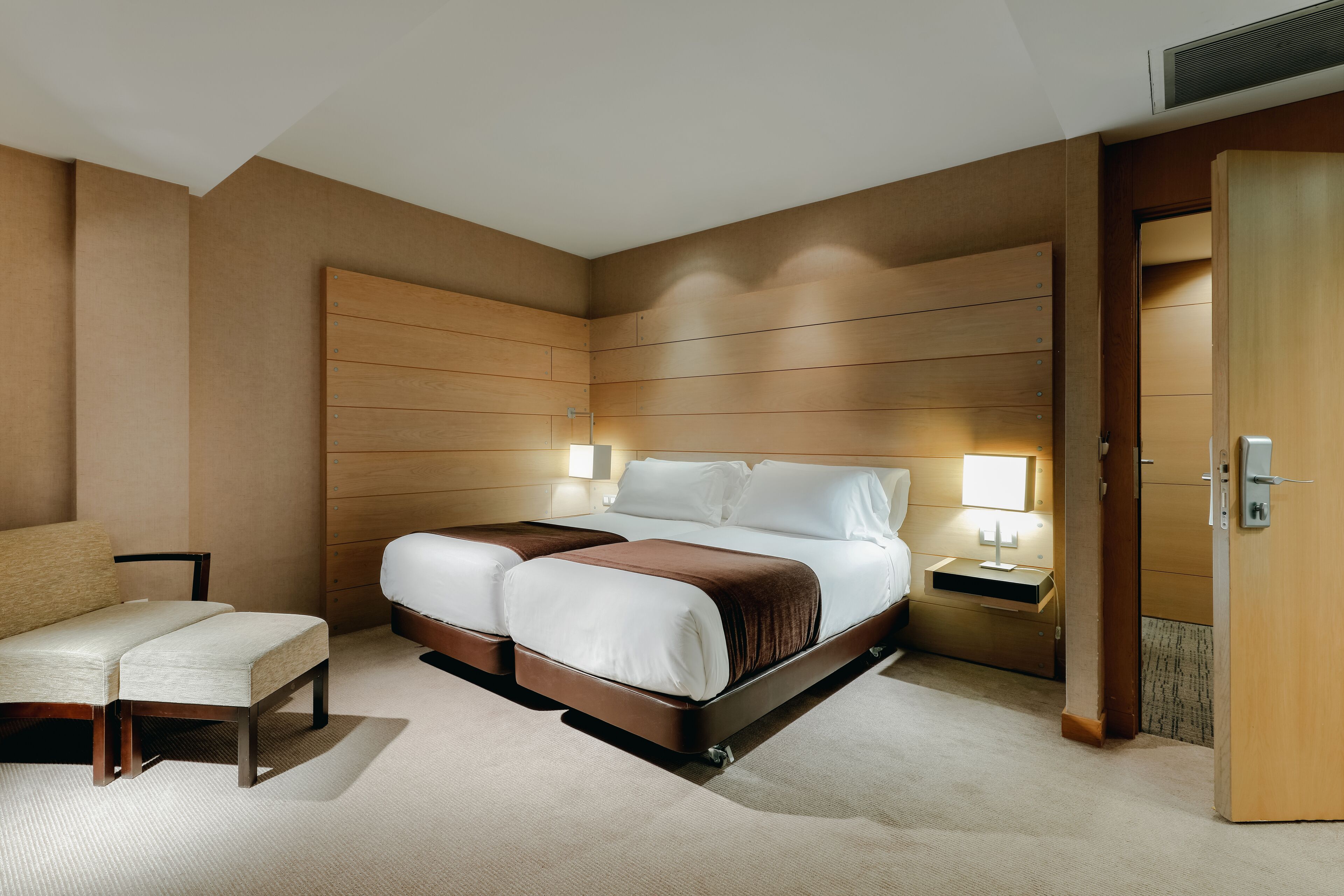 Une chambre d’hôtel moderne avec un grand lit, une table de chevet, une chaise et une armoire en bois.
