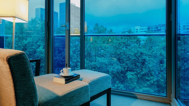 Una habitación moderna con un ventanal grande, un sofá, una lámpara y una mesita con una taza y un libro.