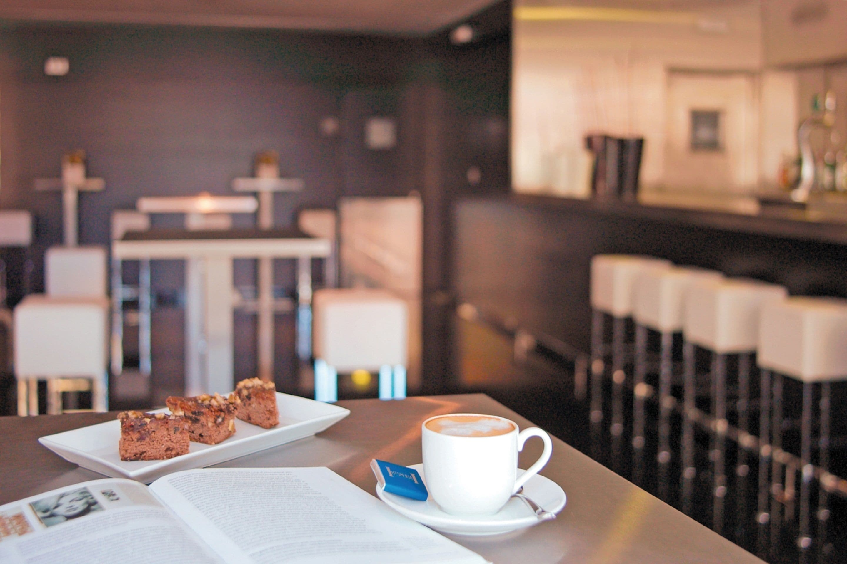 Una mesa con un libro, un plato de comida y una taza de café en un café moderno.