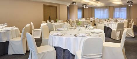 Un salón de banquetes con mesas redondas, sillas blancas y candelabros.