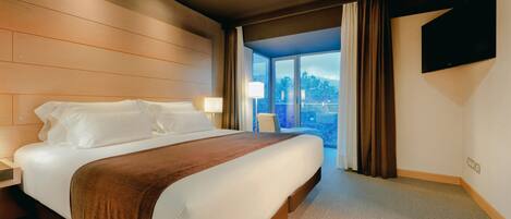Ein Hotelzimmer mit einem großen Bett, einem Flachbildfernseher und Blick ins Freie durch ein großes Fenster.