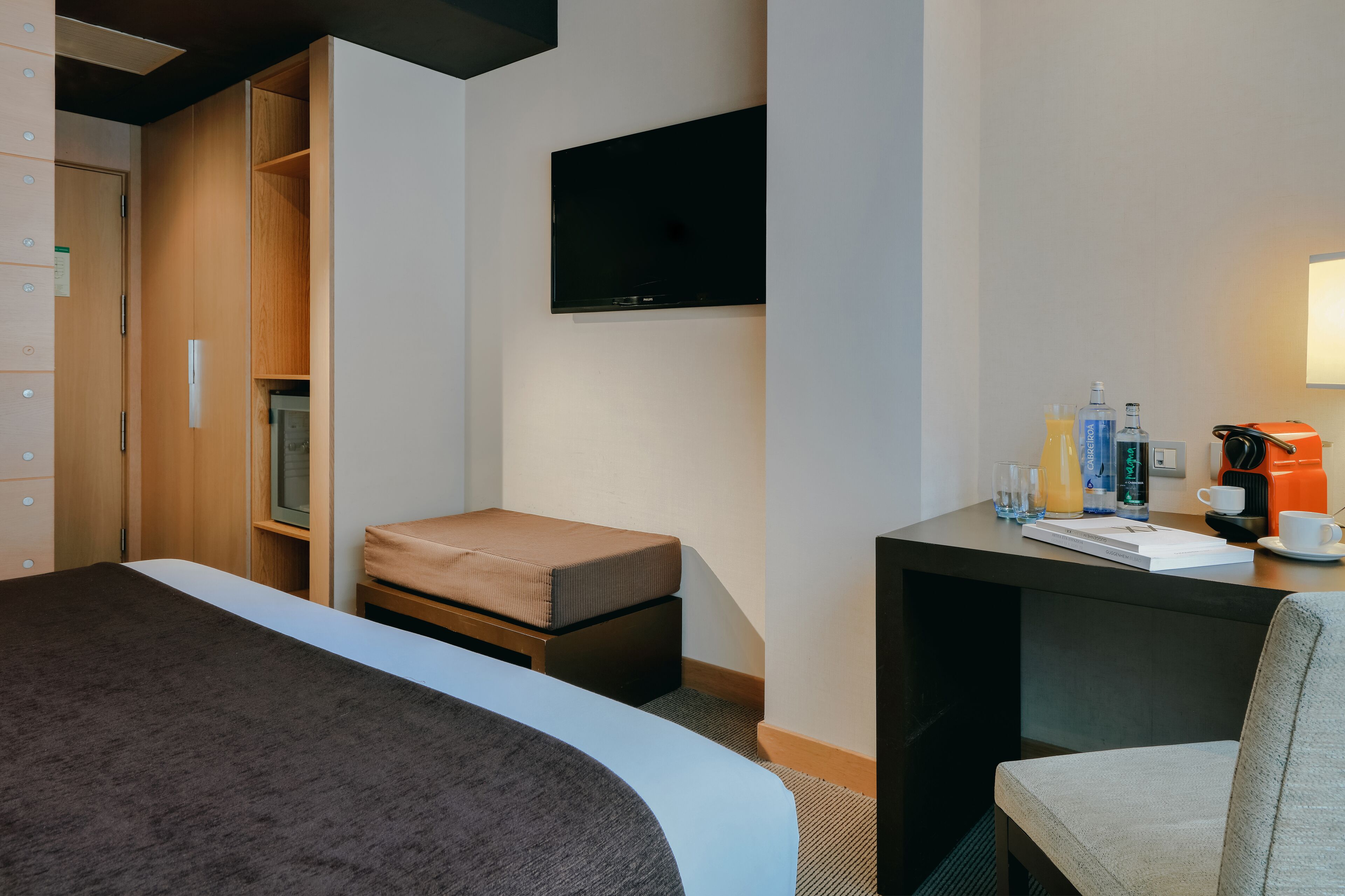 Ein Hotelzimmer mit einem Bett, einem kleinen Schreibtisch mit Kaffeemaschine, einem an der Wand montierten Fernseher und einem Kleiderschrank.