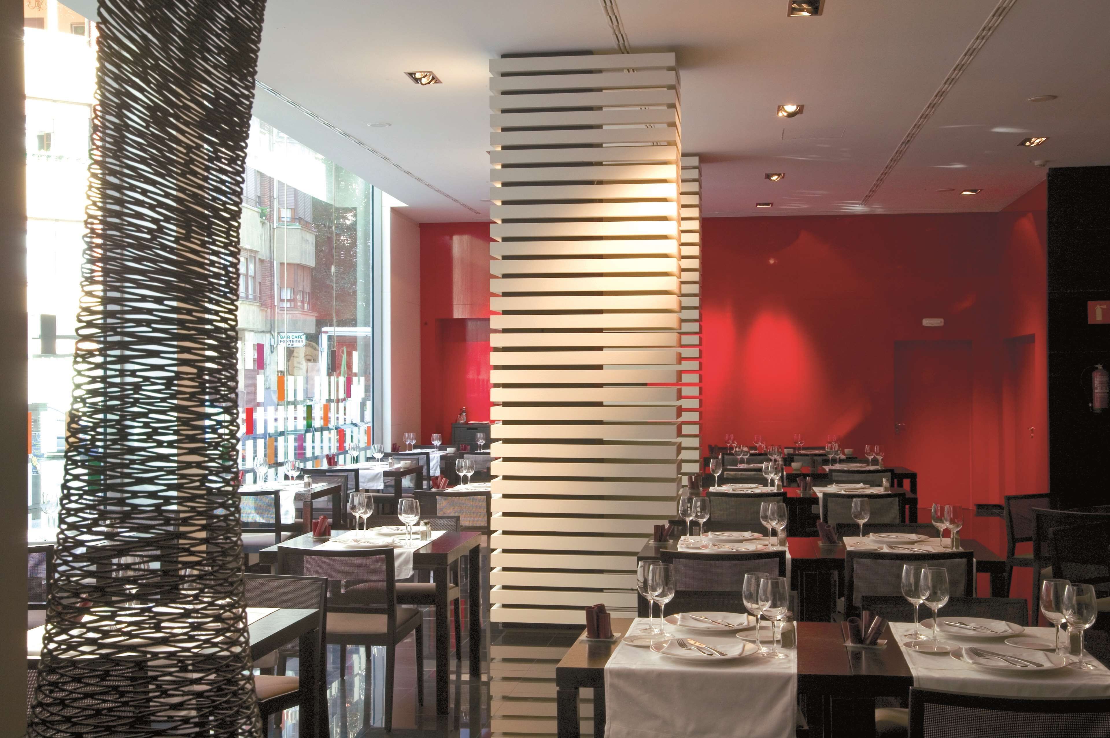 A restaurant with multiple tables, some with wine glasses and cutlery, and a modern, red-walled interior.