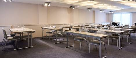 A conference room with multiple tables and chairs, equipped with microphones and glasses.