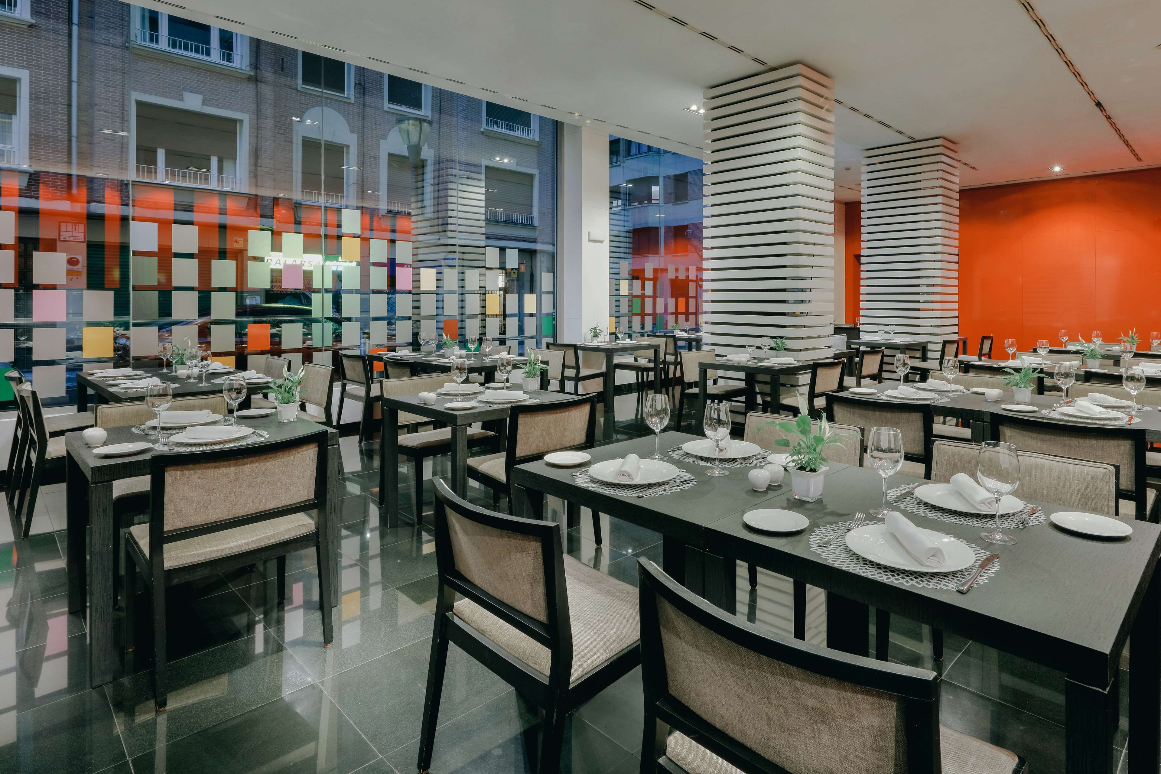 Un restaurante moderno con varias mesas dispuestas para comensales, con una decoración de diseño contemporáneo y amplios ventanales que ofrecen vistas del paisaje urbano.