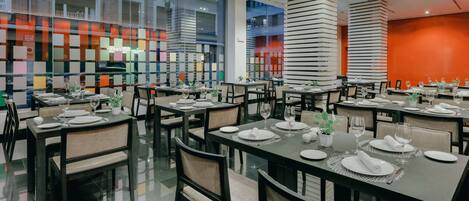 Un restaurante moderno con varias mesas dispuestas para comensales, con una decoración de diseño contemporáneo y amplios ventanales que ofrecen vistas del paisaje urbano.