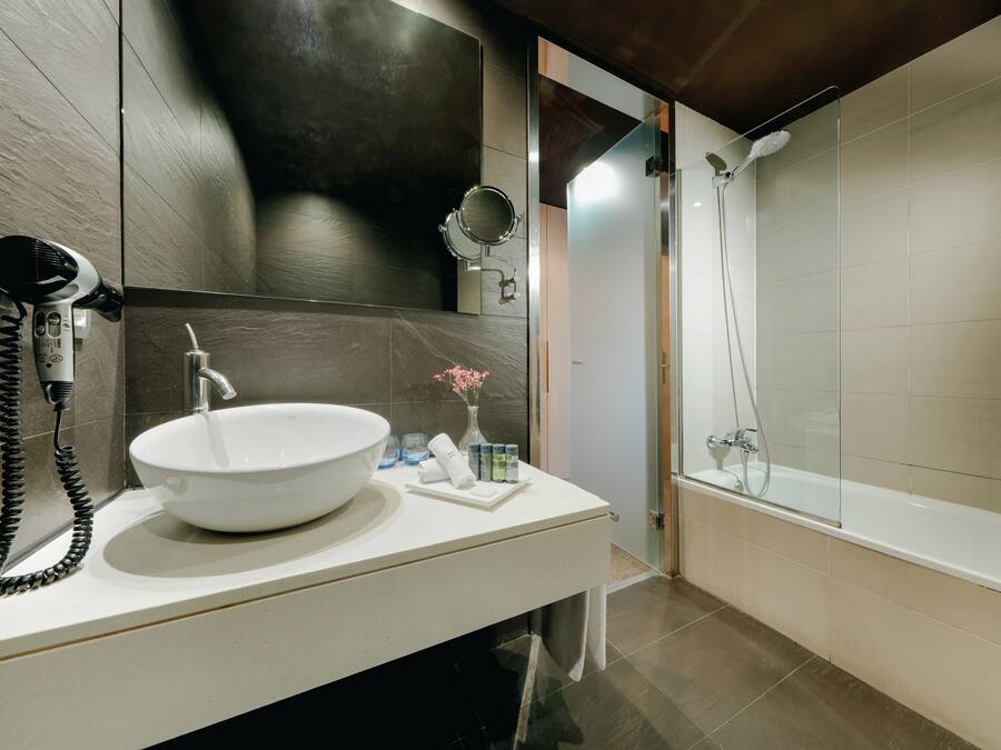 A modern bathroom with a large white sink, a hairdryer, a mirror, and a shower area.