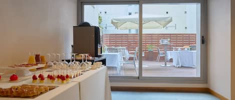 A breakfast buffet with various food items and beverages, a large window with a view of the outdoor seating area.