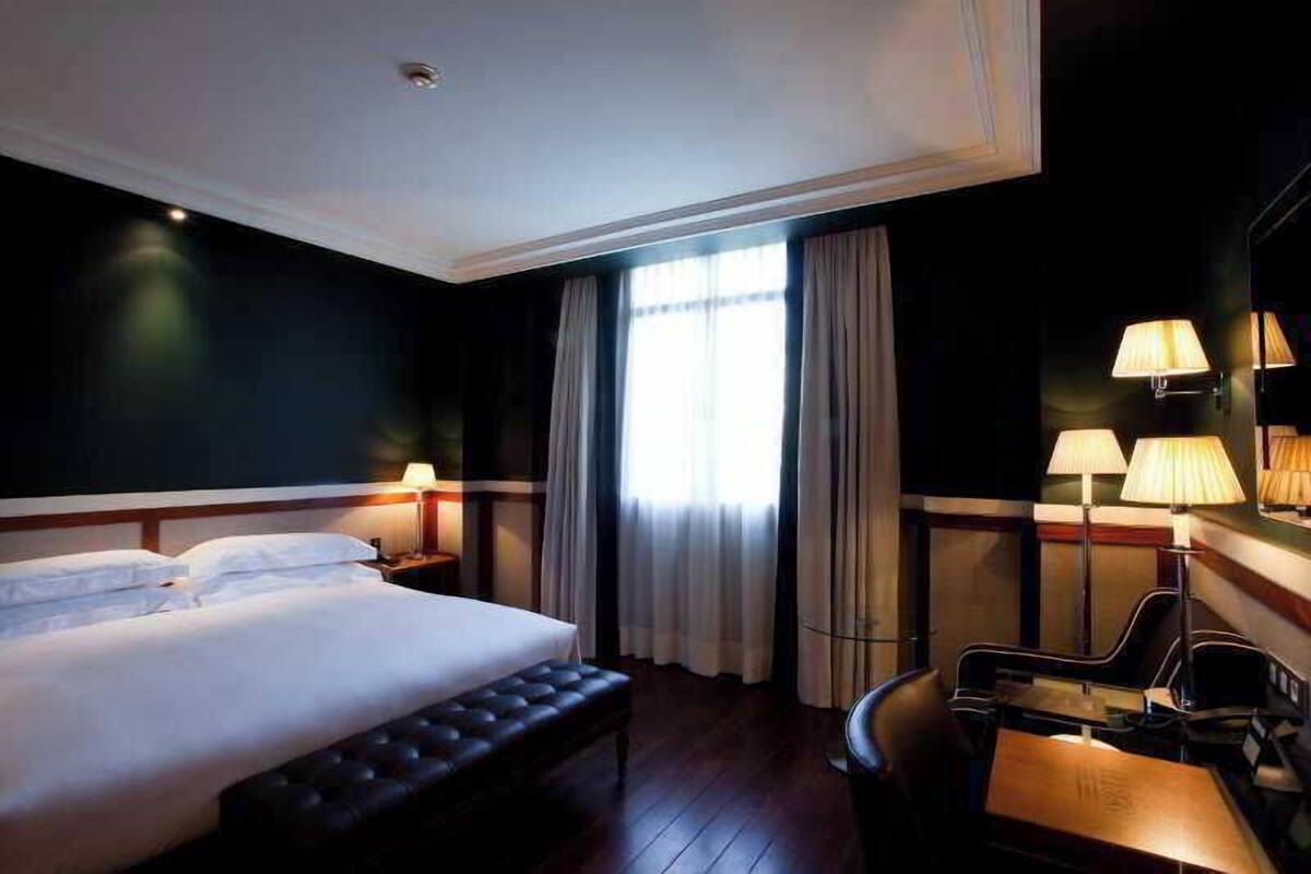A hotel room with a large bed, a desk with a chair, and a window with curtains.