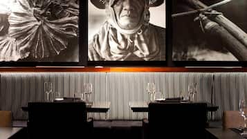 Un restaurante con una pared a rayas, un cuadro enmarcados de una persona con sombrero, y una cuerda atada a una viga de madera.