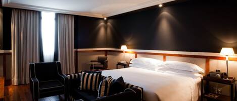 A hotel room with a large bed, two bedside tables with lamps, a chair, and a small table.