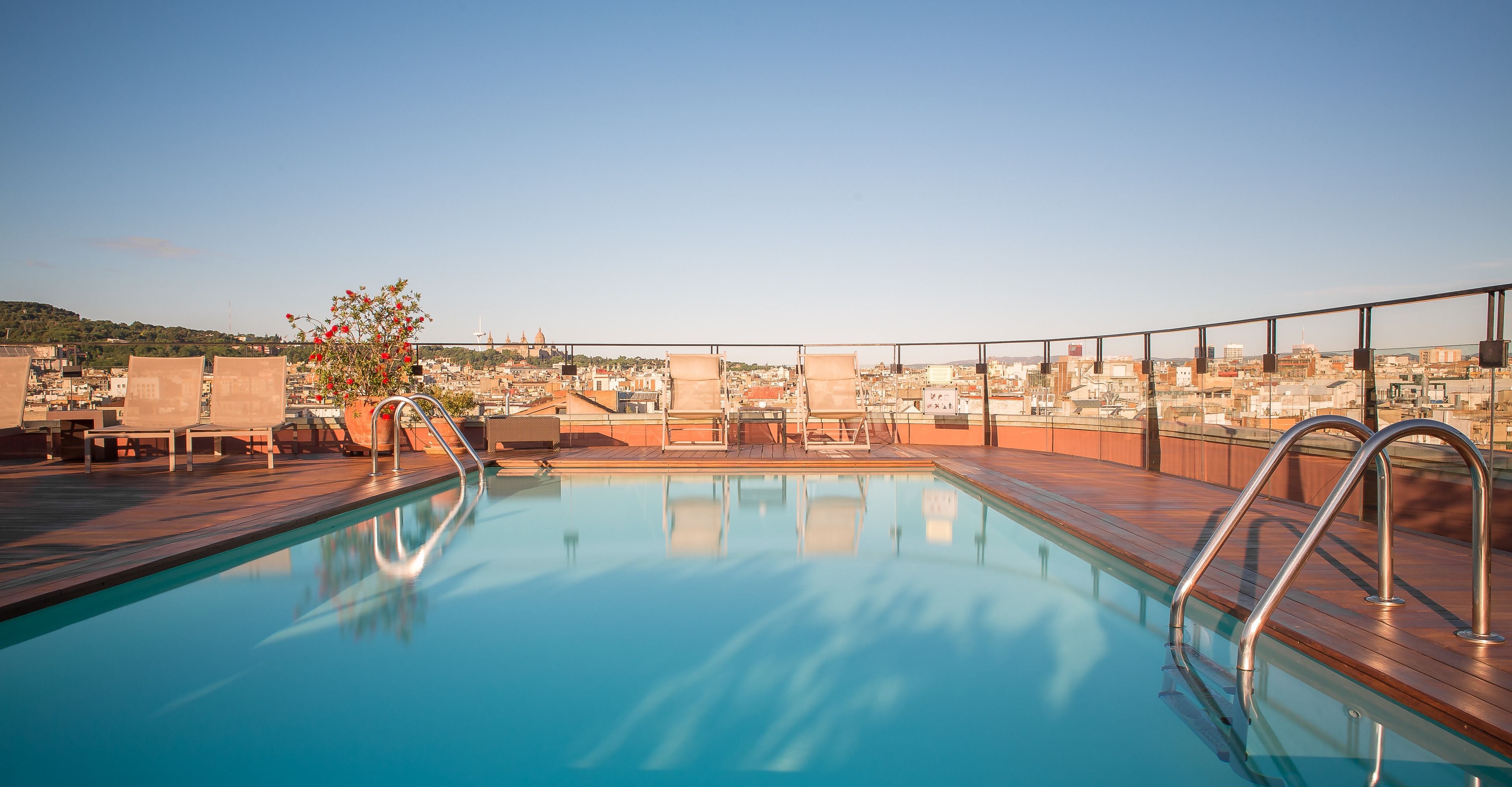 Ein Pool auf dem Dach mit freiem Blick auf die Stadtlandschaft, einschließlich Gebäude und einer Hügelkette in der Ferne.