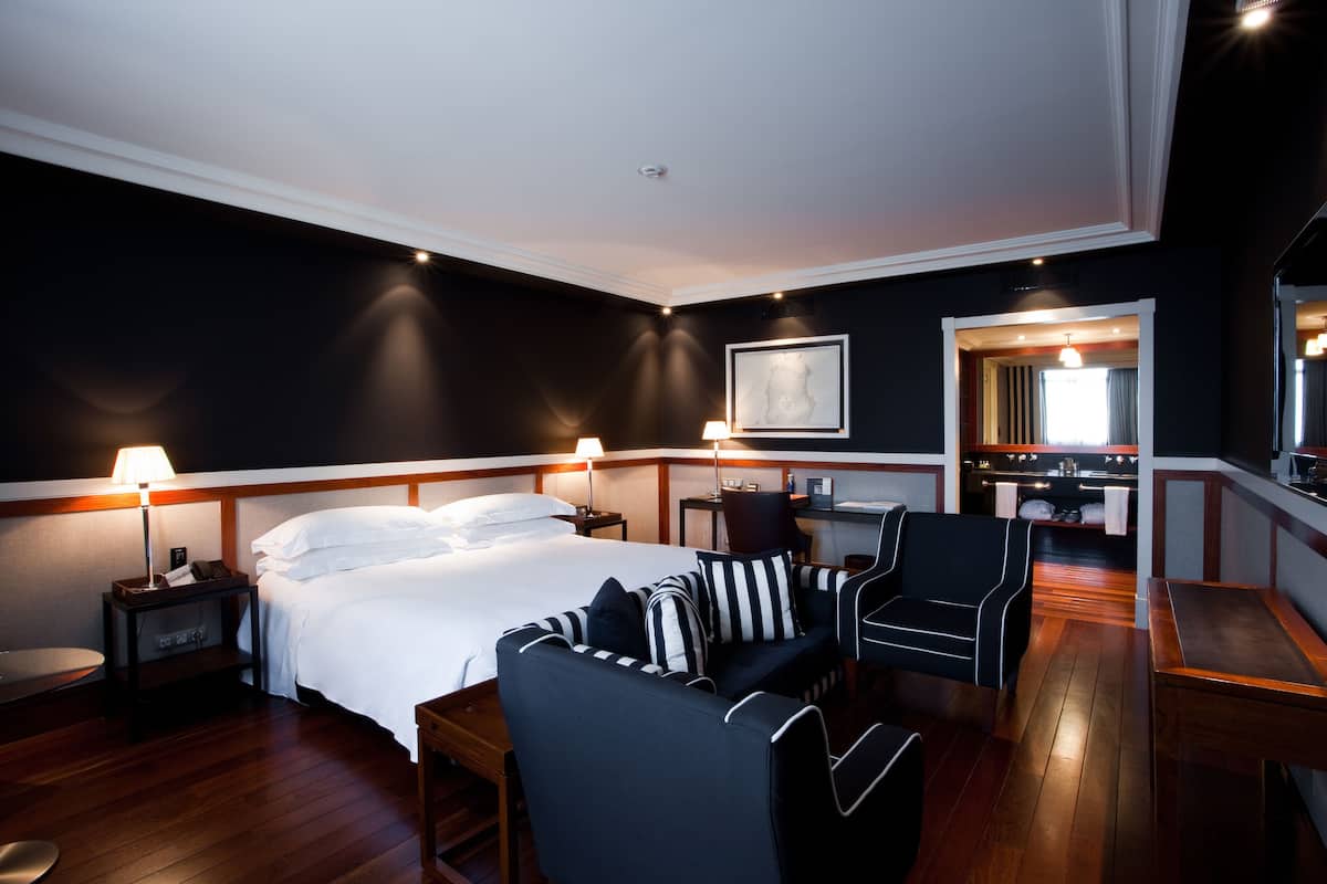 A hotel room with a bed, a sofa, a desk, and a mirror.