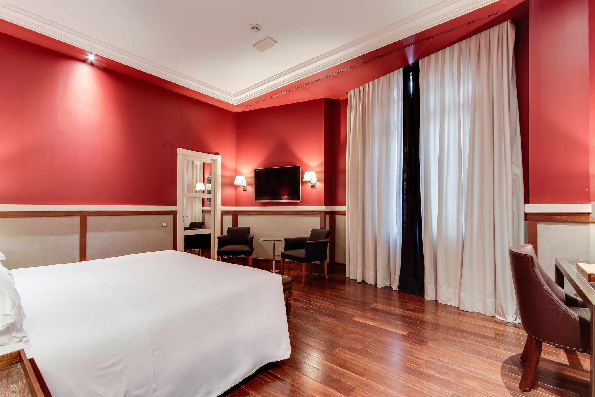 Una habitación de hotel con una cama grande, un escritorio con dos sillas, un televisor y una ventana con cortinas.