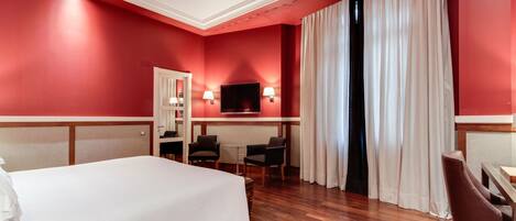 A hotel room with a large bed, a desk with two chairs, a television, and a window with curtains.