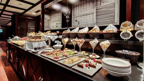 A buffet with various food items and drinks, including pastries, fruits, and desserts, displayed on a counter with a decorative wall in the background. - Hotel 1898 (Barcelona)