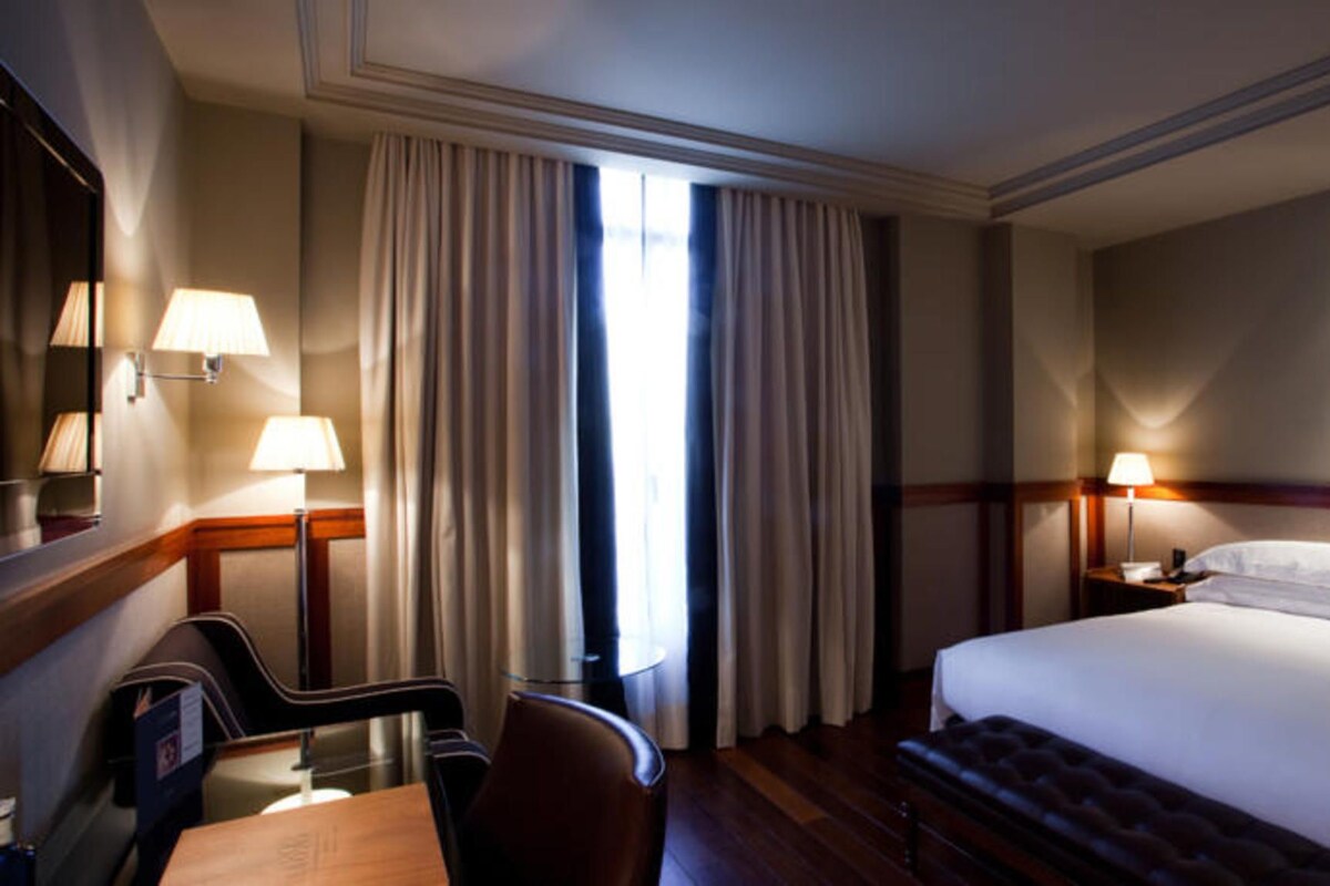 Hotellihuone, jossa on suuri sänky, työpöytä tuolilla, peili ja kaksi lamppua.