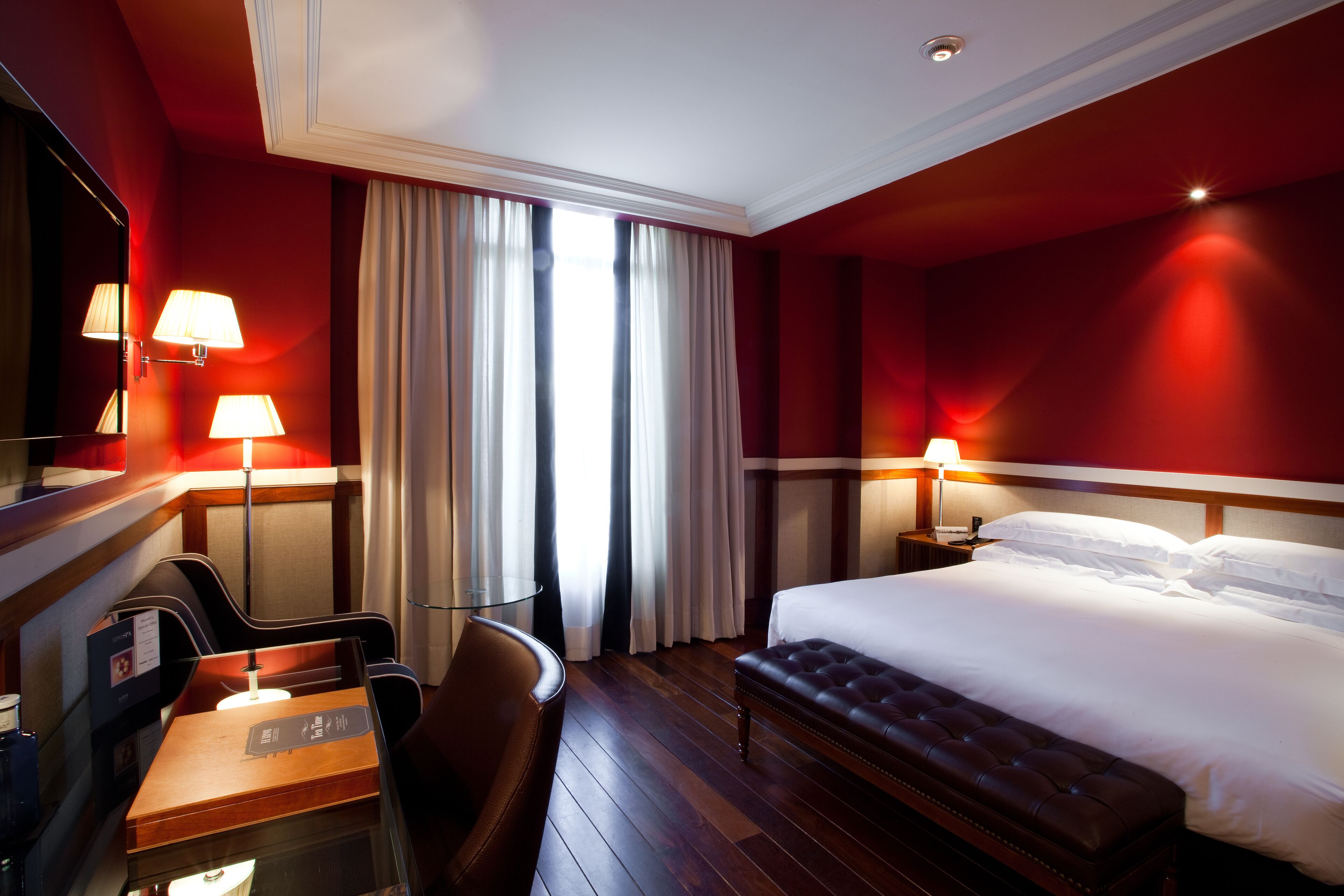Une chambre d’hôtel avec un grand lit, deux lampes de chevet, un bureau avec une chaise et une grande fenêtre avec des rideaux.