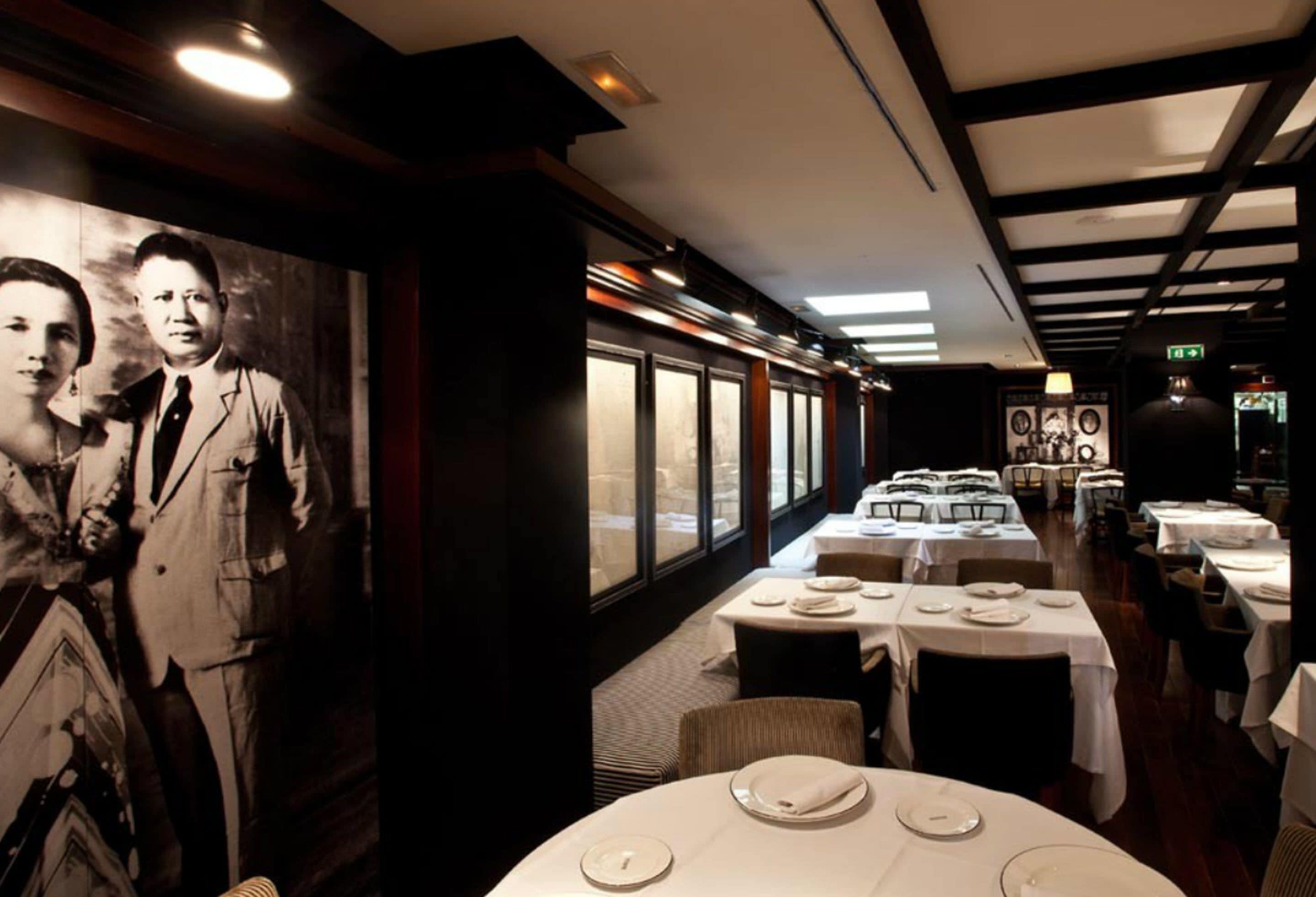 En restaurang med dukade bord, ett stort svartvitt fotografi på väggen och en utsikt genom fönstren.