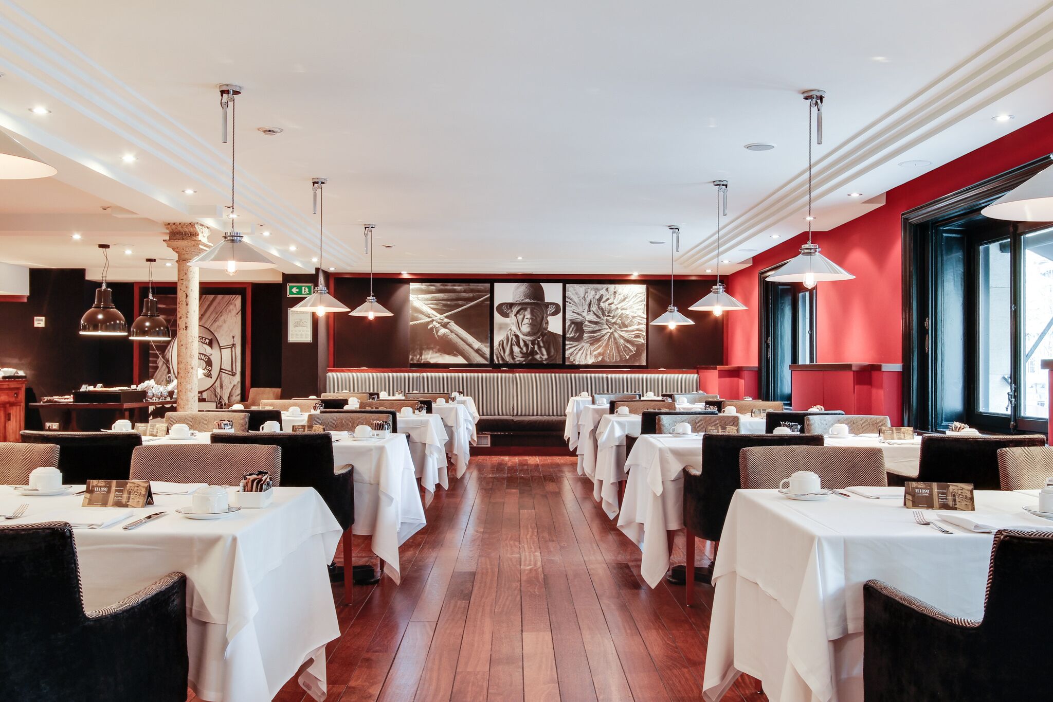 A restaurant with white tablecloths, black chairs, and pendant lighting.