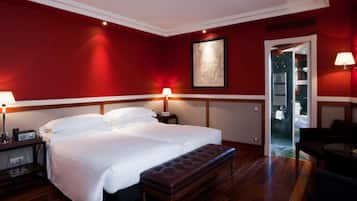A hotel room with a large bed, two bedside lamps, a wooden bench, and a red wall.