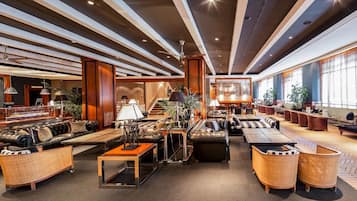 A spacious lobby with leather sofas, a central coffee table, and a staircase leading to upper floors.
