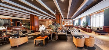A spacious lobby with leather sofas, a central coffee table, and a staircase leading to upper floors.