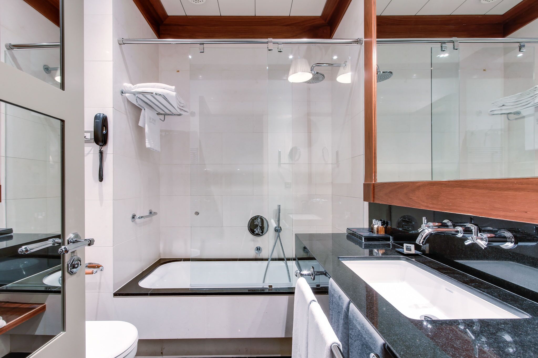 A modern bathroom with a glass-enclosed shower, a bathtub, and a vanity with a black countertop.