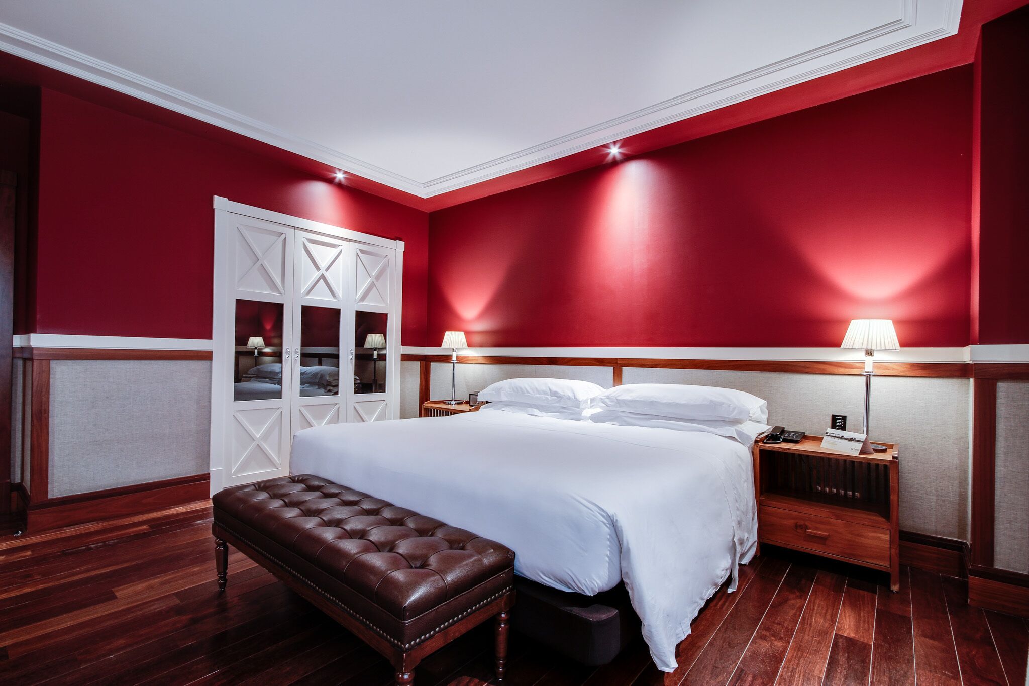 A hotel room with a large bed, wooden nightstands, a bench, and a wardrobe with a mirror.