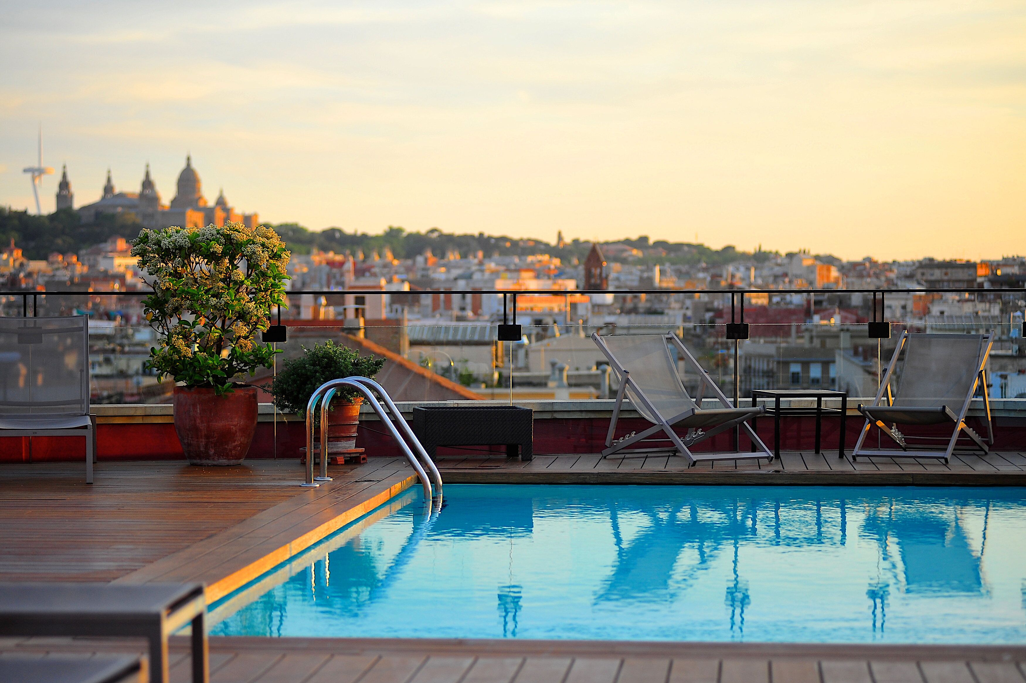 Piscina no terraço com espreguiçadeiras e uma planta em vaso, com vista para um horizonte urbano com edifícios históricos.