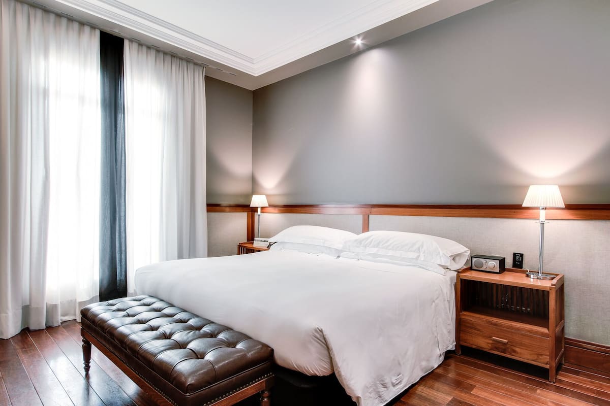 A neatly arranged hotel room with a large bed, a wooden bench, two bedside tables with lamps, and a nightstand with a radio.