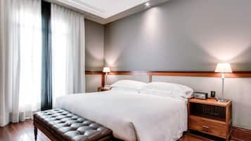 Una habitación de hotel impecable, con una cama grande, un banco de madera, dos mesitas de noche con lámparas y un atril con una radio.