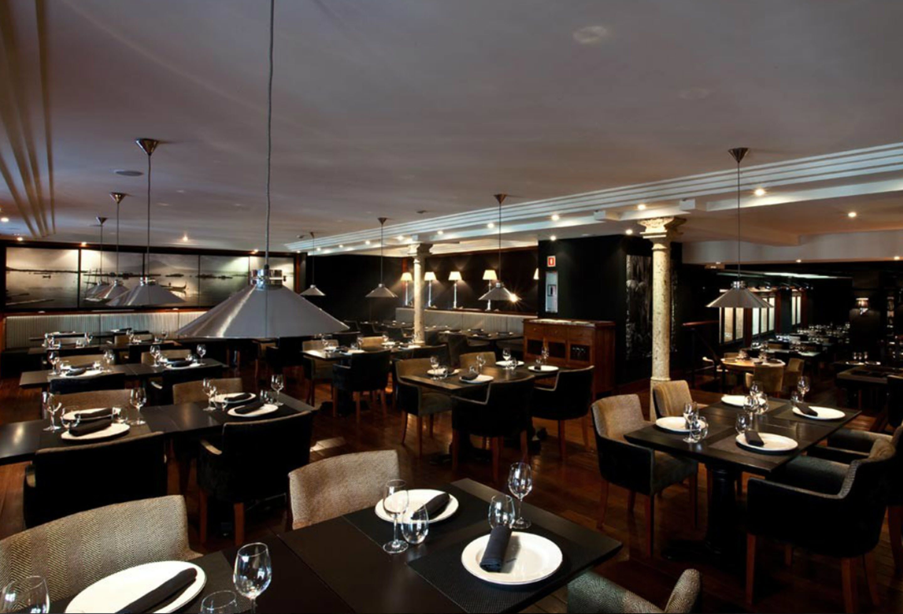 Un restaurante con varias mesas, sillas y una amplia zona de cocina al fondo.