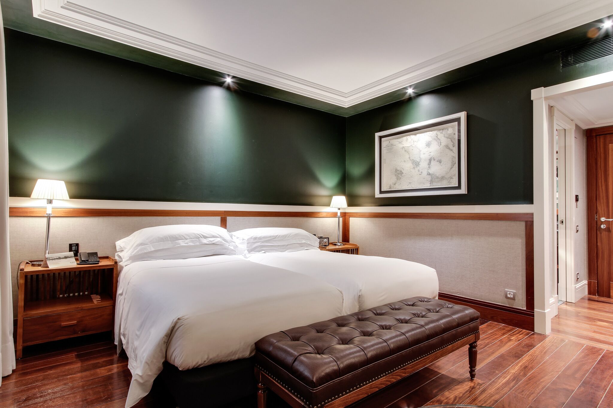 A neatly arranged bedroom with a large bed, bedside lamps, a wooden bench, and a framed artwork on the wall.
