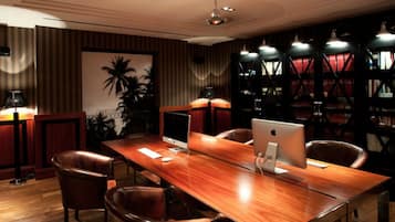 Un salón de conferencias con una mesa de madera, sillas de cuero y dos computadoras Apple iMac.
